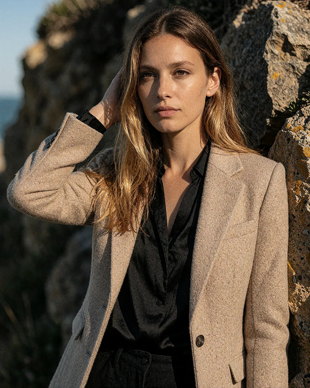 Alba Vidaurre trägt einen beigen Blazer über schwarzer Bluse an einer Felsküste.