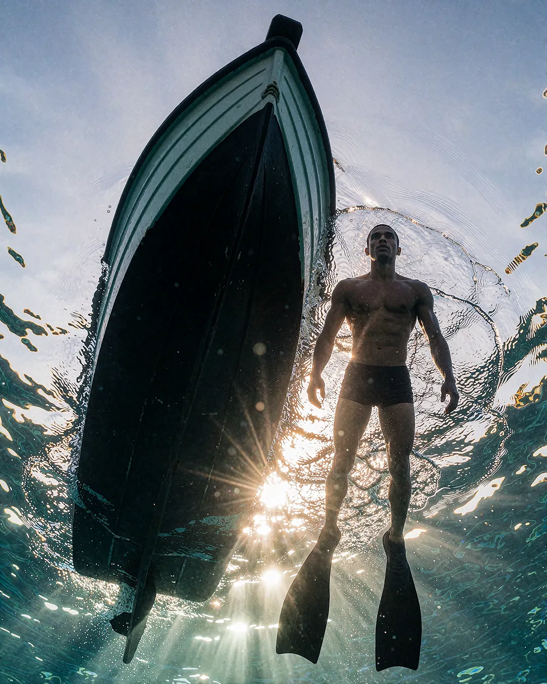 Baptiste Marchois schwimmt mit Flossen im Gegenlicht neben einem Boot unter Wasser.