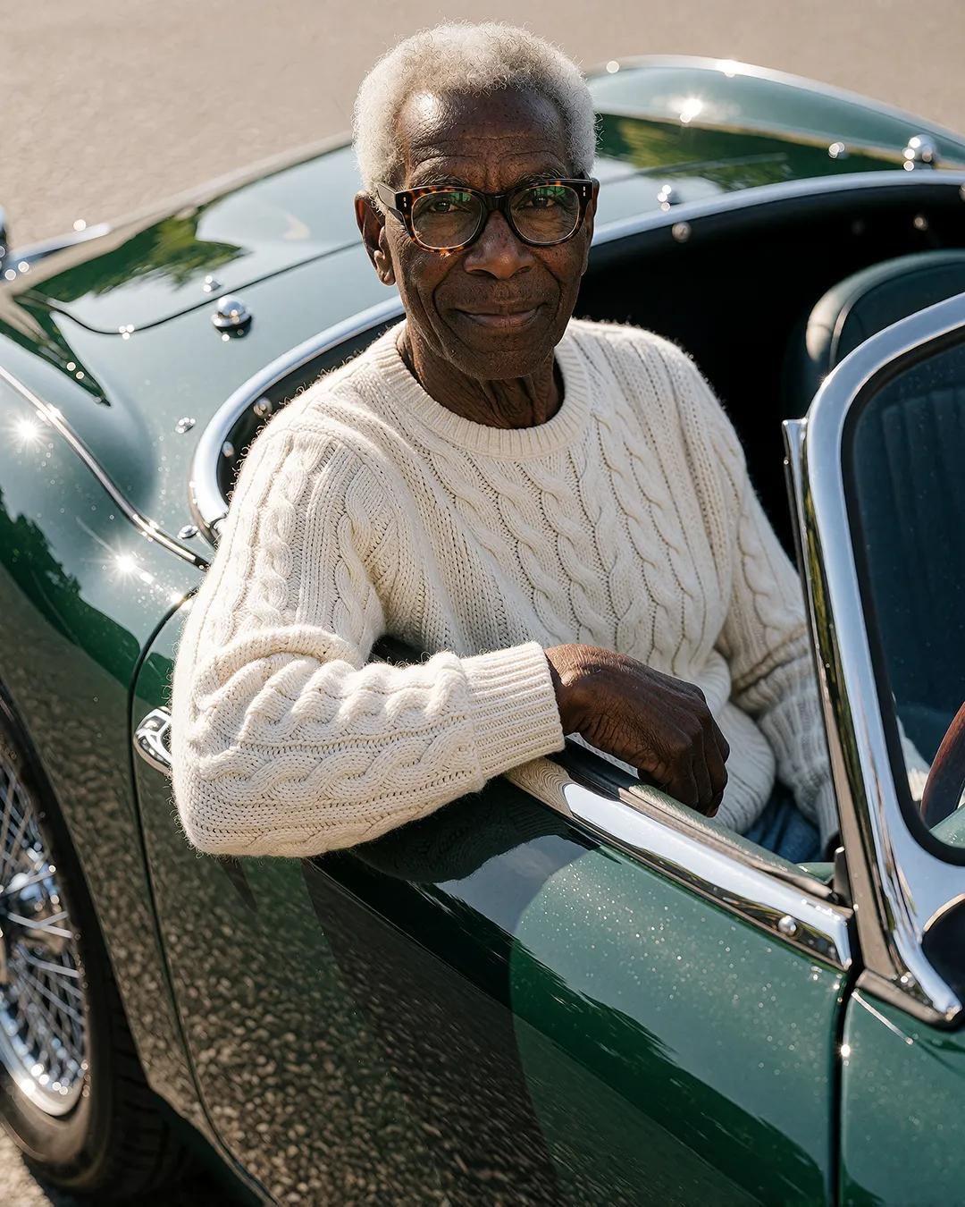 Earl Radcliffe lehnt lächelnd aus einem grünen Cabrio-Sportwagen im cremefarbenen Zopfpullover.