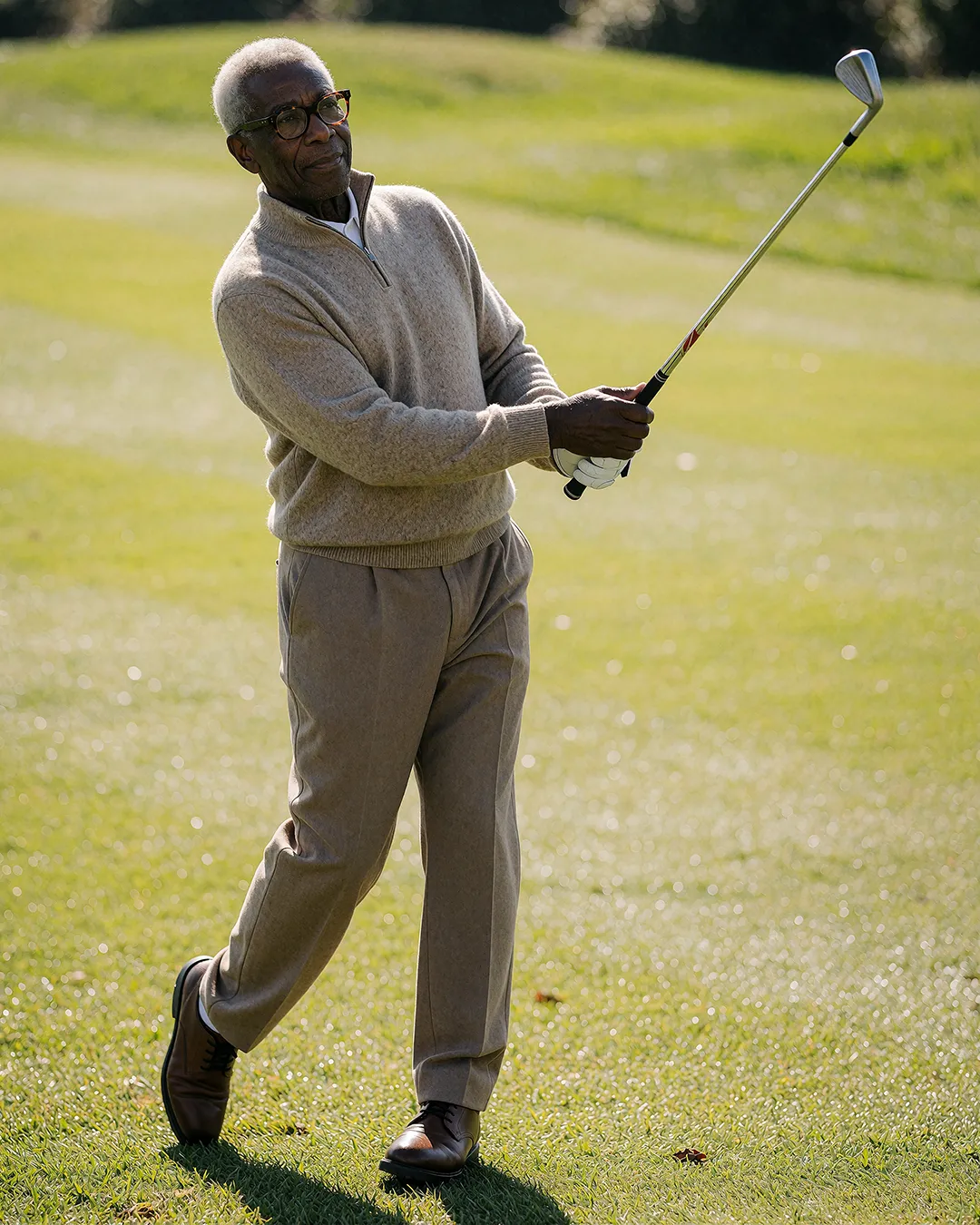 Earl Radcliffe schwingt konzentriert den Golfschläger im beigen Pullover auf dem Golfplatz.