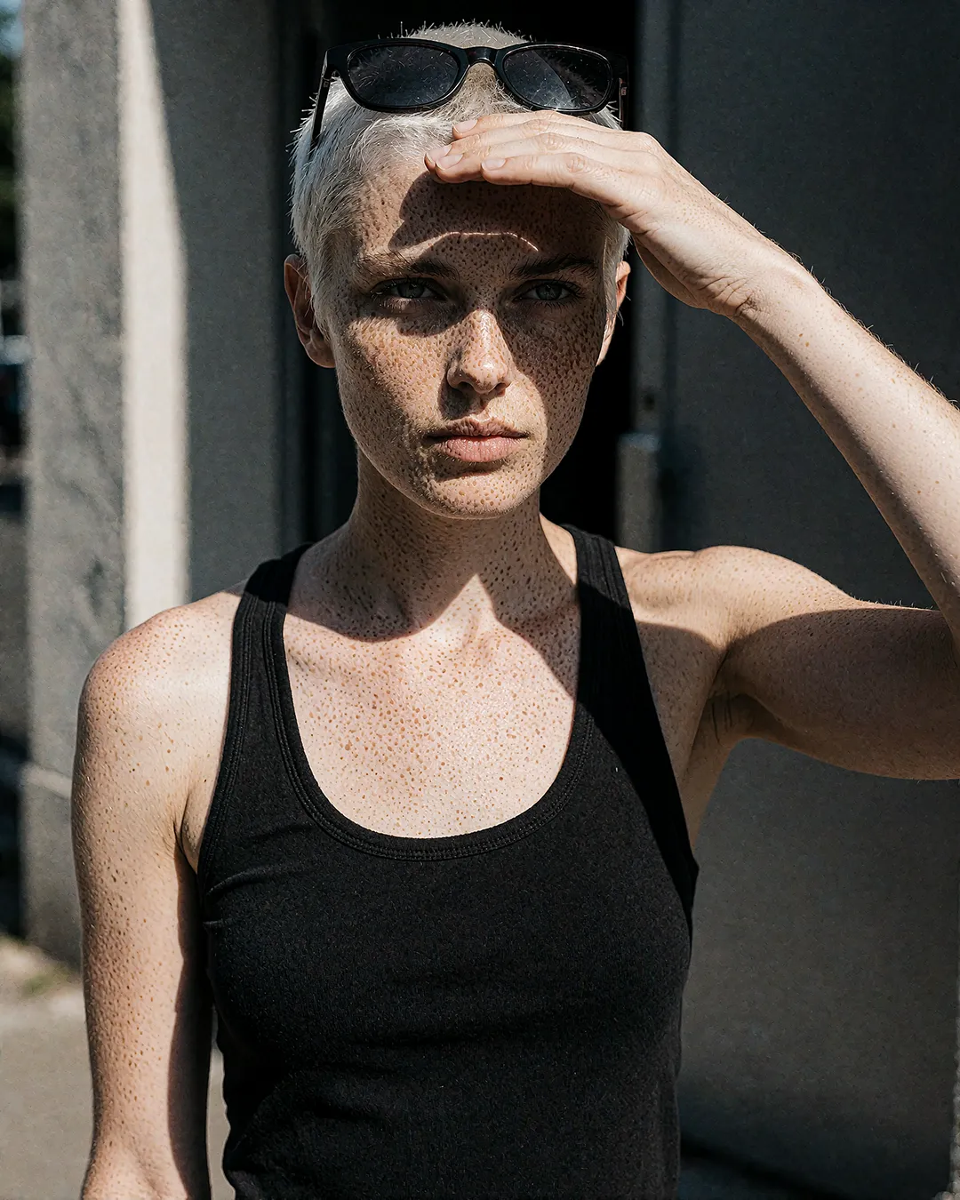 Robin Aschenberg blickt in die Sonne, urbanes Editorial-Porträt mit Sonnenbrille und Sommersprossen.