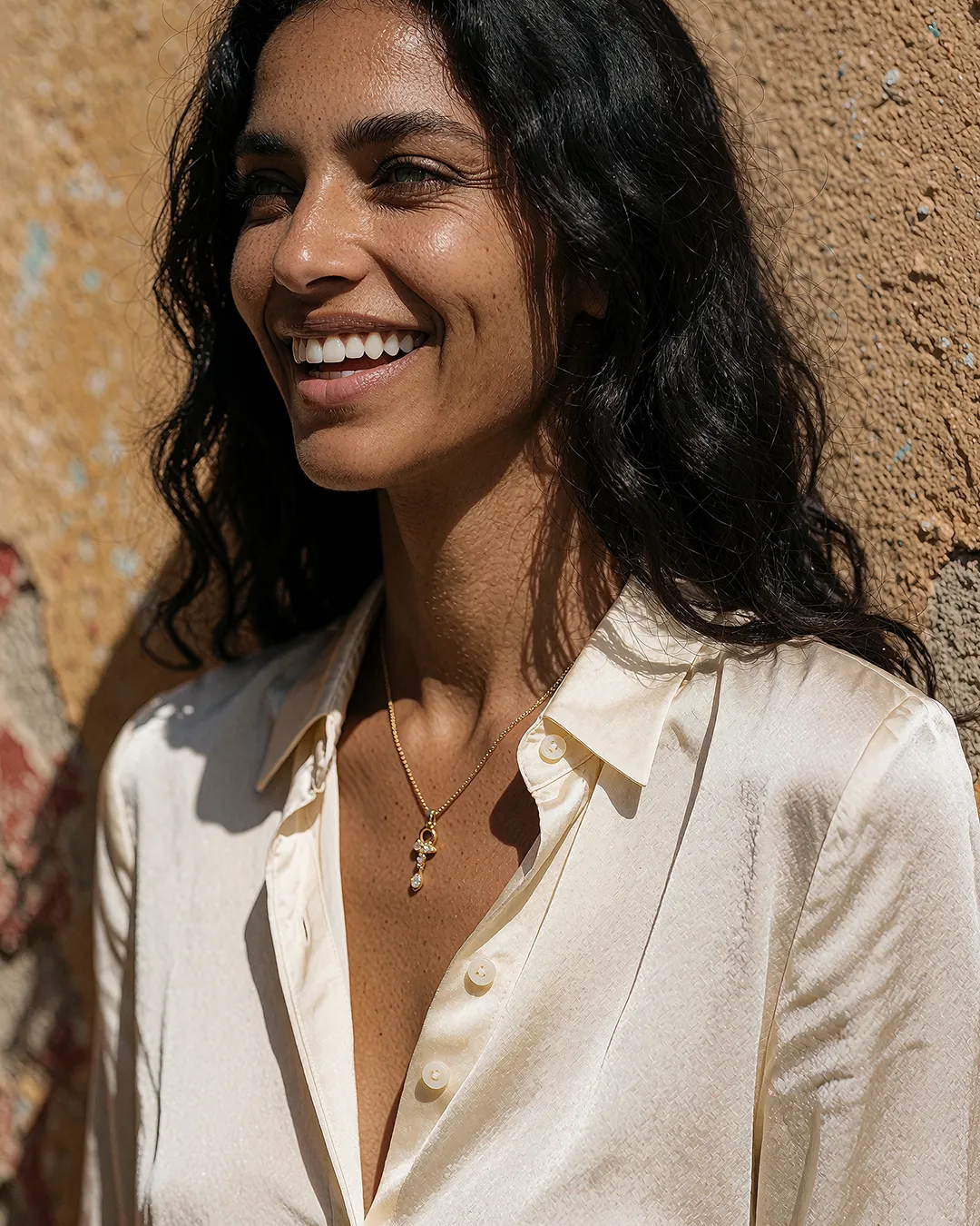 Samira Farrouk im Porträt mit beigefarbener Seidenbluse vor einer ockerfarbenen Wand.
