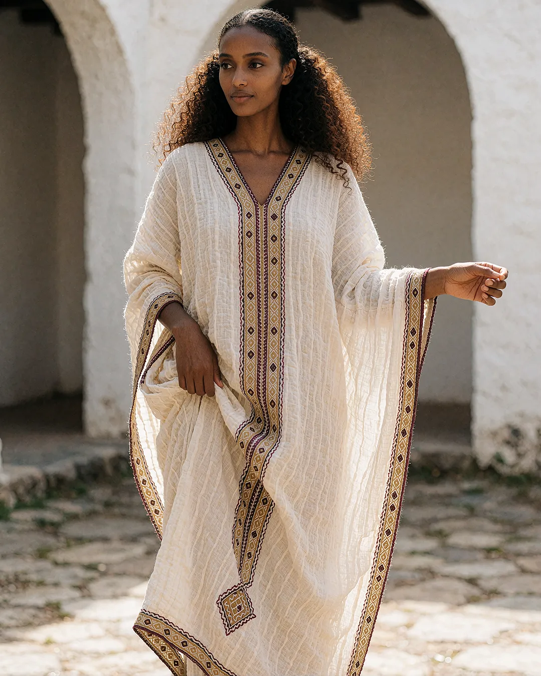 Zuri Osei trägt einen bestickten cremefarbenen Kaftan in einem mediterranen Bogenhof.