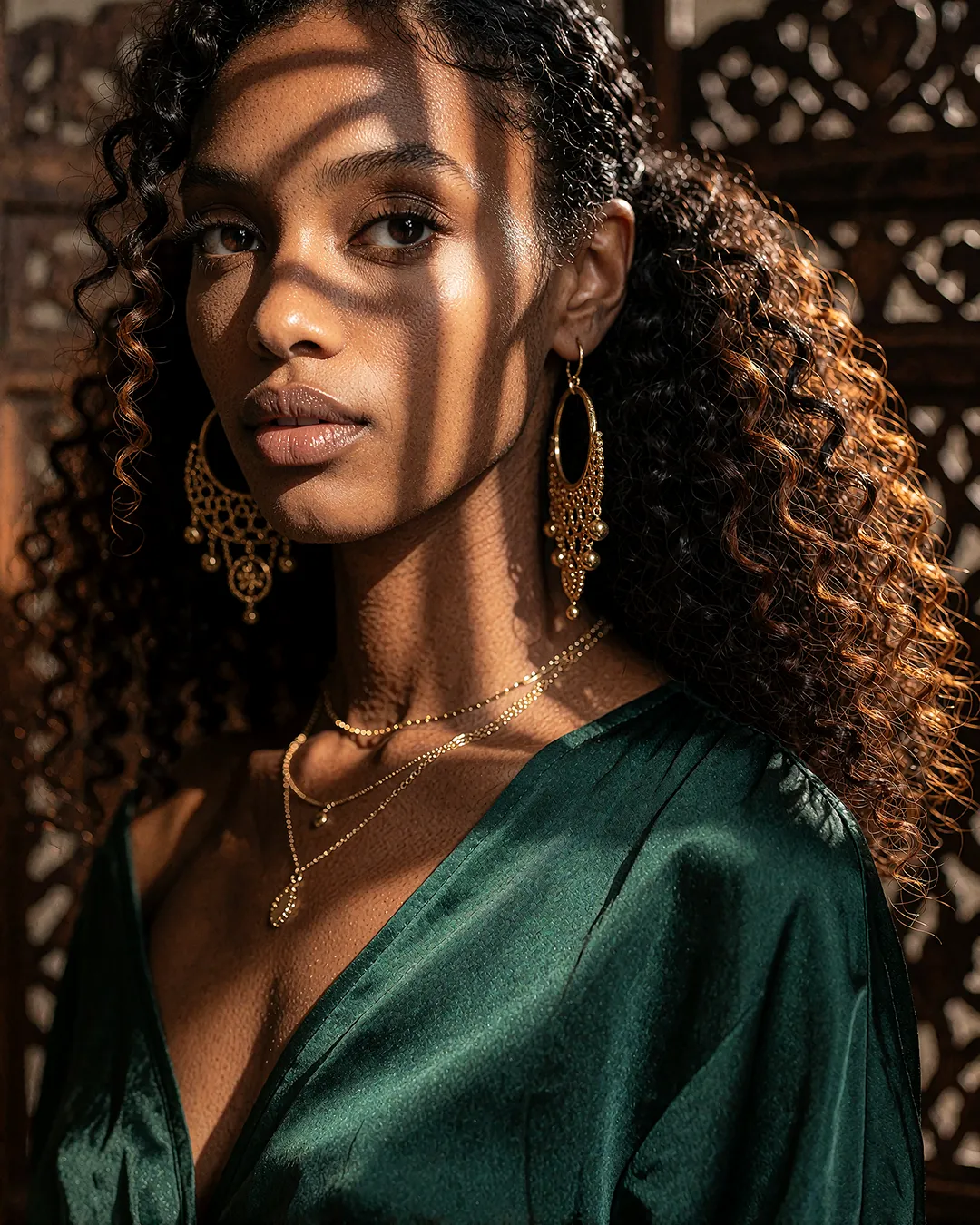Zuri Osei im Beauty-Porträt mit smaragdgrünem Satintop und goldenem Schmuck im Streiflicht.