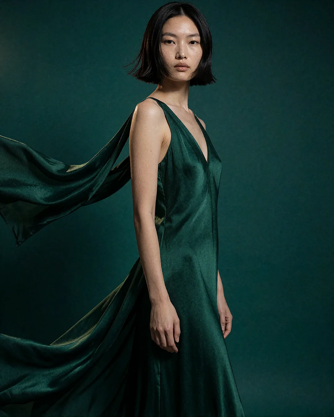 Nanami Onodera trägt ein fließendes smaragdgrünes Seidenkleid mit wehender Schleppe im Studio.