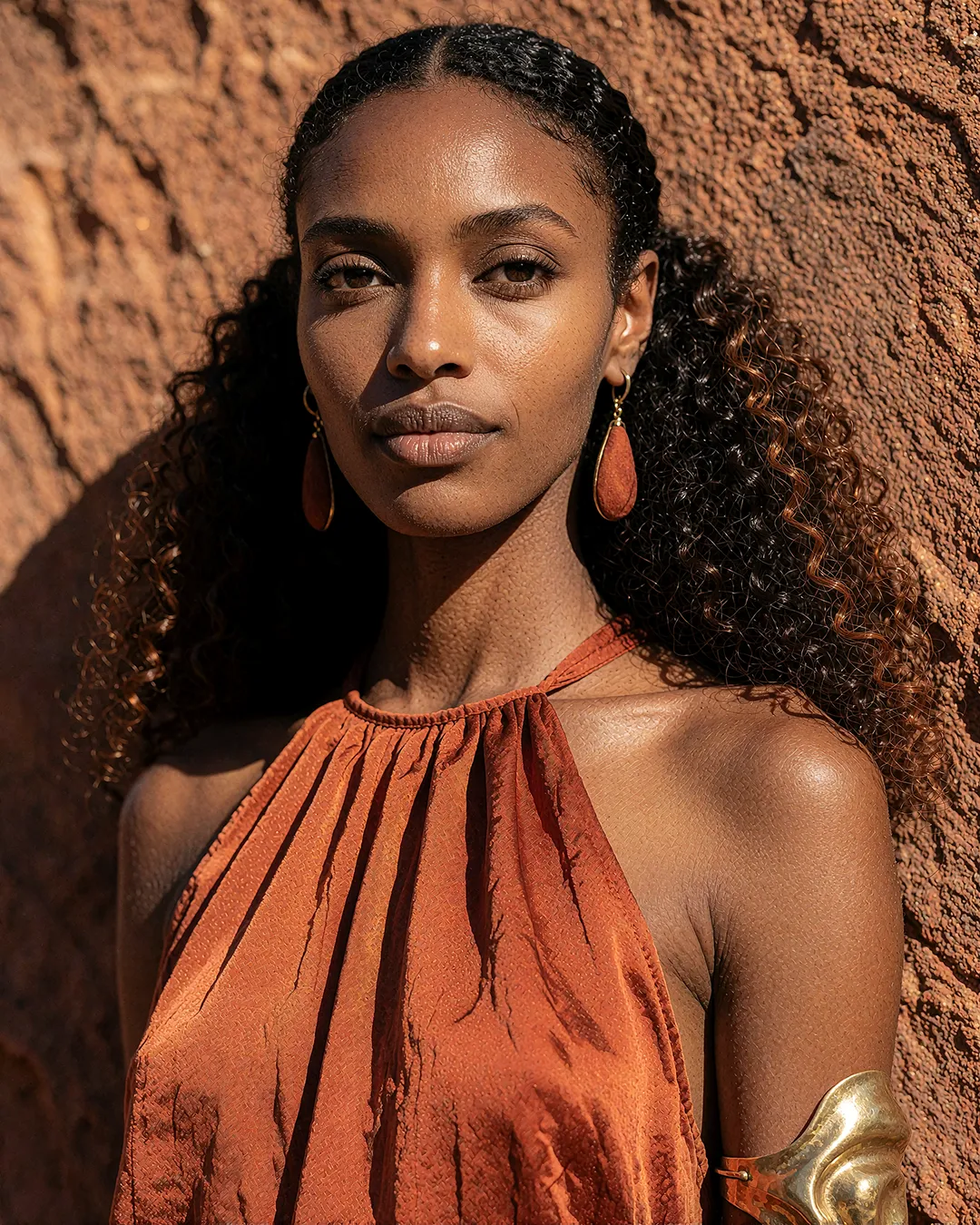 Zuri Osei im Beauty-Porträt mit rostfarbenem Satintop vor einer roten Felswand.