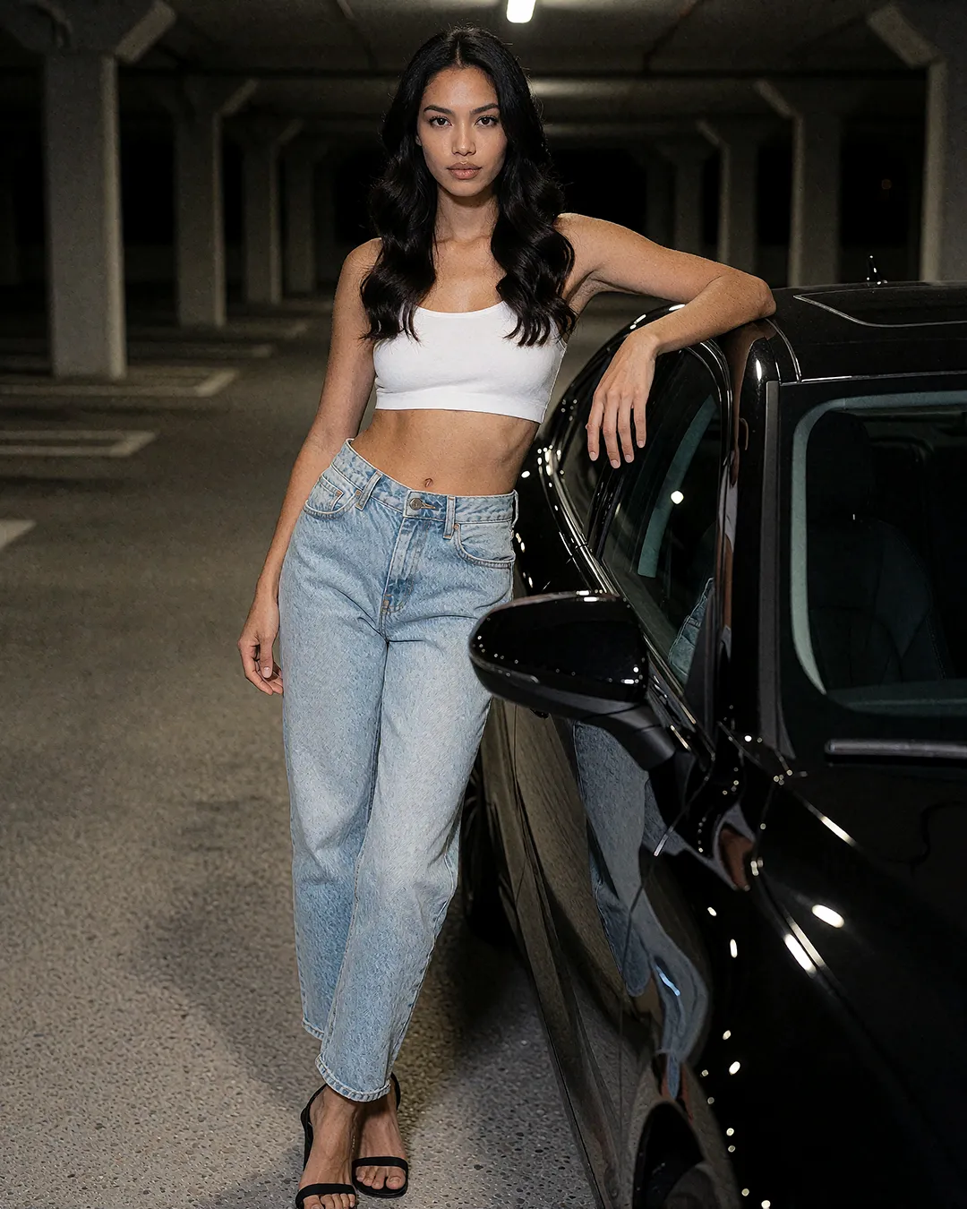 Mika Thornbury lehnt in weißem Crop-Top und Jeans lässig an einem schwarzen Auto im Parkhaus.