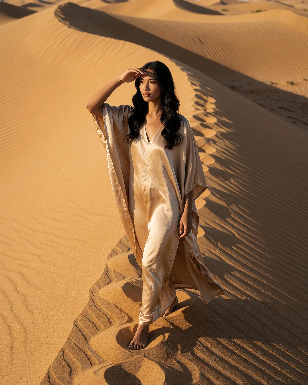 Mika Thornbury trägt einen champagnerfarbenen Seiden-Kaftan in den goldenen Wüstendünen.