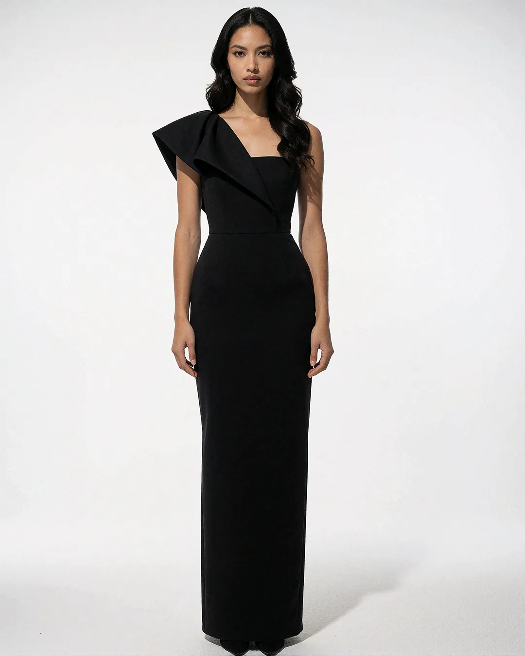 Mika Thornbury trägt ein schwarzes Abendkleid mit skulpturaler Schulterrüsche im weißen Studio.