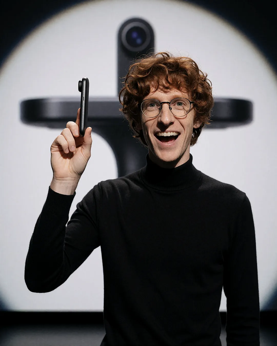 Tobias Osterhage präsentiert lachend ein neues Smartphone vor futuristischem Kamerastativ.