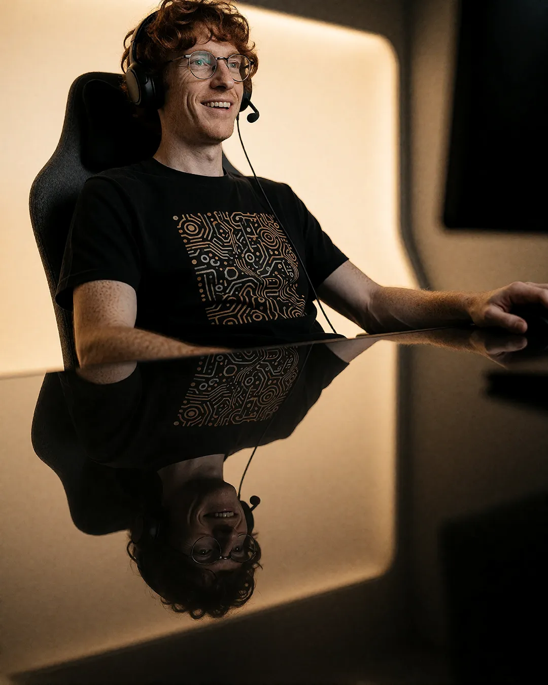 Tobias Osterhage trägt ein Gaming-Headset lächelnd an einem spiegelnden Schreibtisch.