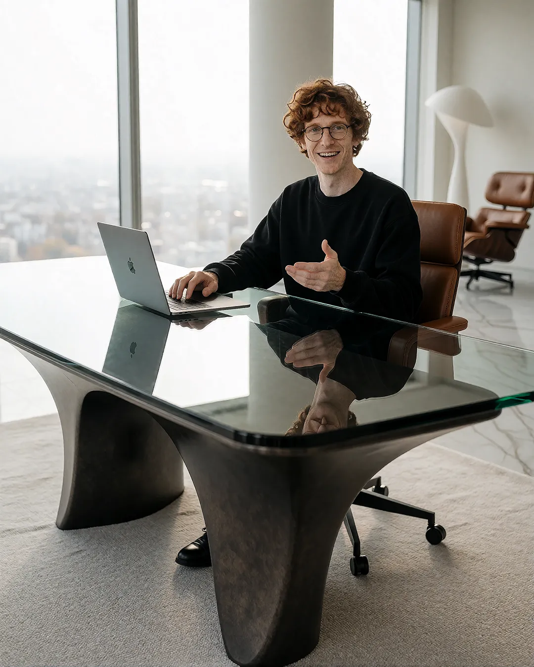 Tobias Osterhage sitzt lächelnd mit Laptop an einem Glastisch mit Blick über die Stadt.