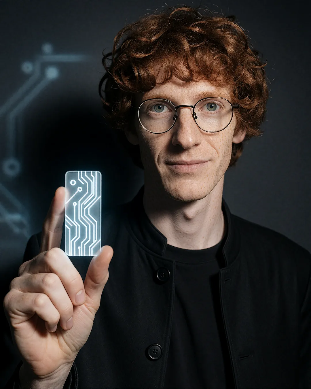 Tobias Osterhage hält eine leuchtende digitale Schaltkreis-Karte vor dunklem Hintergrund.